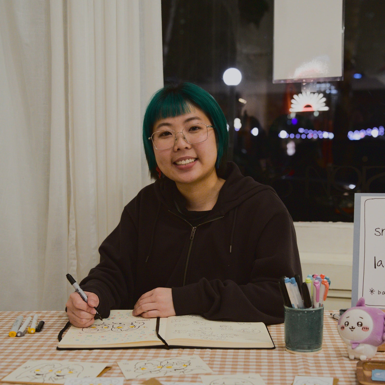 Lily sitting at a table with a checkered tablecloth, drawing in a sketchbook.